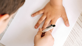 Lapsi piirtää toisen lapsen kättä