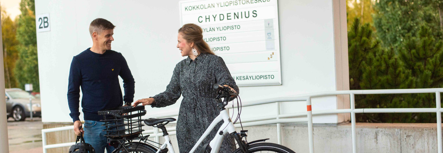 kaksi opiskelijaa pyörän kanssa pihalla